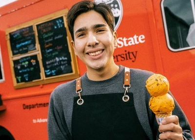 Student holding an icecream cone standing in front of the Beaver Classic food truck. Photo by Karl Maasdam, '93